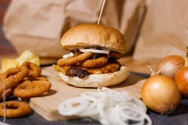 Obraz Burger w artystycznej kompozycji z frytkami i batatami oraz cebulą pieczarkami. Burgerownia - zdjęcie świeżego, apetycznego burgera