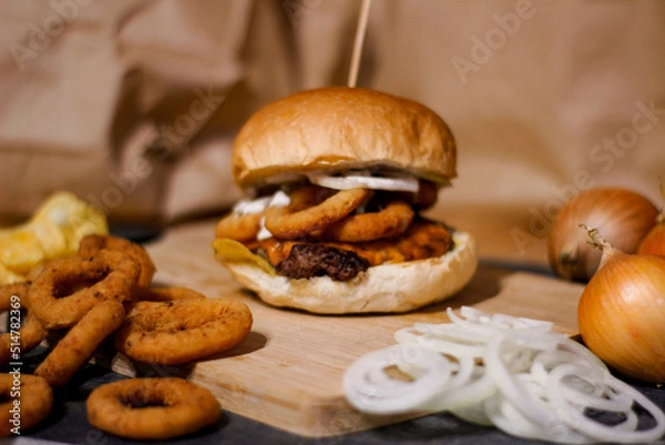 Obraz Burger w artystycznej kompozycji z frytkami i batatami oraz cebulą pieczarkami. Burgerownia - zdjęcie świeżego, apetycznego burgera