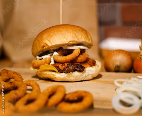 Obraz Burger w artystycznej kompozycji z frytkami i batatami oraz cebulą pieczarkami. Burgerownia - zdjęcie świeżego, apetycznego burgera