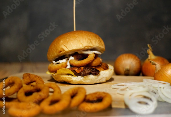 Obraz Burger w artystycznej kompozycji z frytkami i batatami oraz cebulą pieczarkami. Burgerownia - zdjęcie świeżego, apetycznego burgera