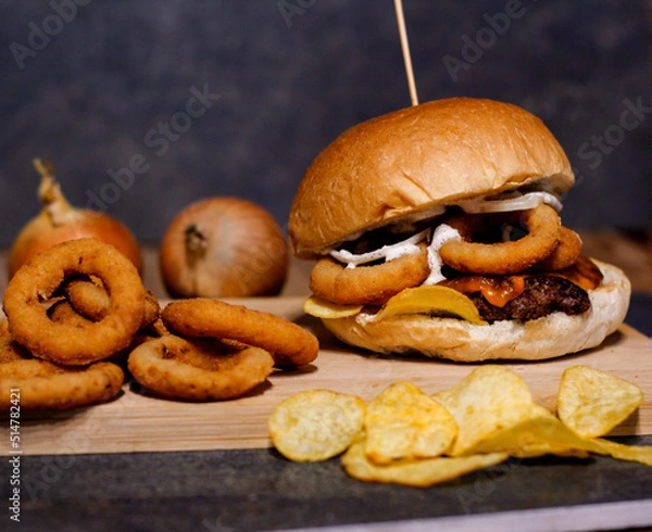 Obraz Burger w artystycznej kompozycji z frytkami i batatami oraz cebulą pieczarkami. Burgerownia - zdjęcie świeżego, apetycznego burgera