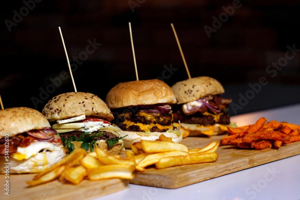 Obraz Burger w artystycznej kompozycji z frytkami i batatami oraz cebulą pieczarkami. Burgerownia - zdjęcie świeżego, apetycznego burgera