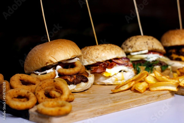 Obraz Burger w artystycznej kompozycji z frytkami i batatami oraz cebulą pieczarkami. Burgerownia - zdjęcie świeżego, apetycznego burgera