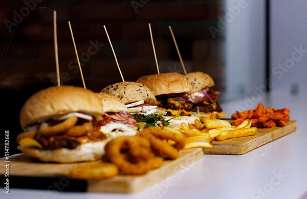 Obraz Burger w artystycznej kompozycji z frytkami i batatami oraz cebulą pieczarkami. Burgerownia - zdjęcie świeżego, apetycznego burgera