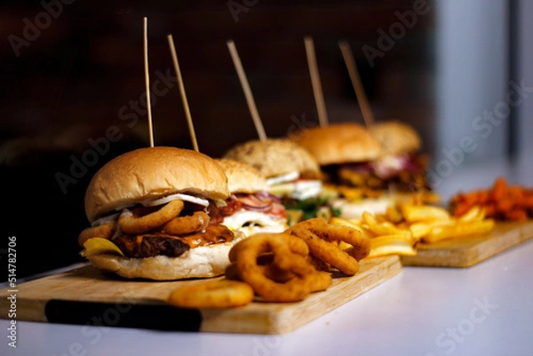 Obraz Burger w artystycznej kompozycji z frytkami i batatami oraz cebulą pieczarkami. Burgerownia - zdjęcie świeżego, apetycznego burgera