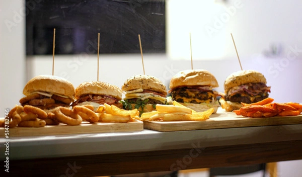 Obraz Burger w artystycznej kompozycji z frytkami i batatami oraz cebulą pieczarkami. Burgerownia - zdjęcie świeżego, apetycznego burgera