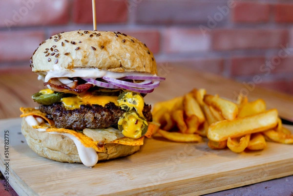 Obraz Burger w artystycznej kompozycji z frytkami i batatami oraz cebulą pieczarkami. Burgerownia - zdjęcie świeżego, apetycznego burgera