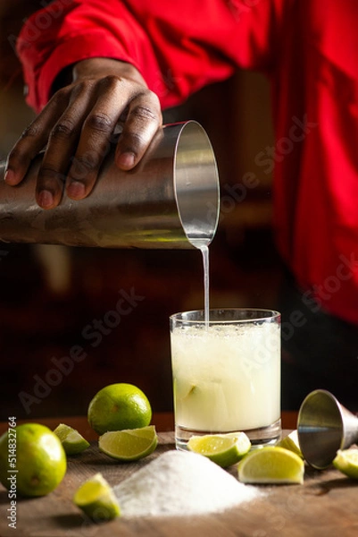 Fototapeta Bartender pouring Brazilian Caipirinha, typical Brazilian cocktail made with lemon, cachaça and sugar on a wooden board
