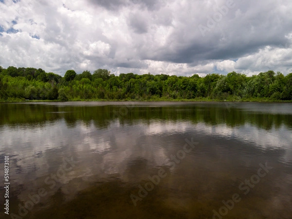 Fototapeta Large clouds are reflected in a small lake in cottage county in Ontario, Canada.