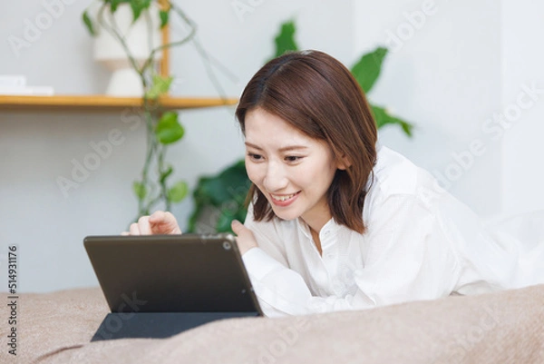 Obraz ベッドで寝転んでタブレットを見る女性