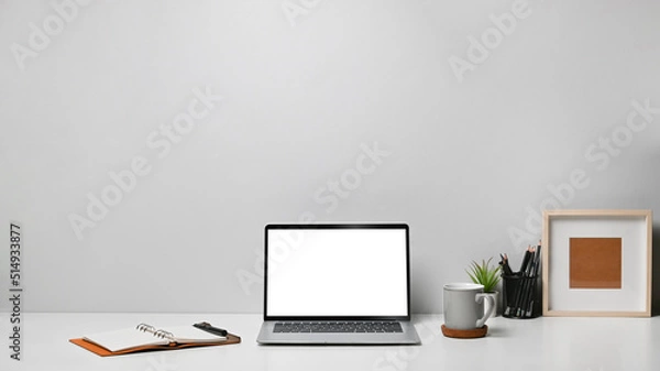 Fototapeta Front view laptop computer, coffee cup, picture frame, notebook and pencil holder on white table