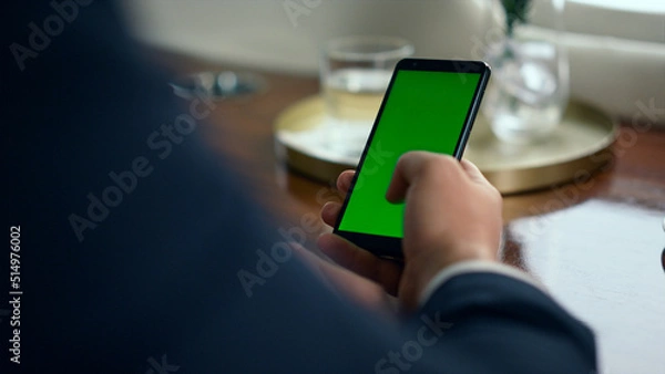 Fototapeta Man hand scrolling green smartphone screen closeup. Businessman using chroma key