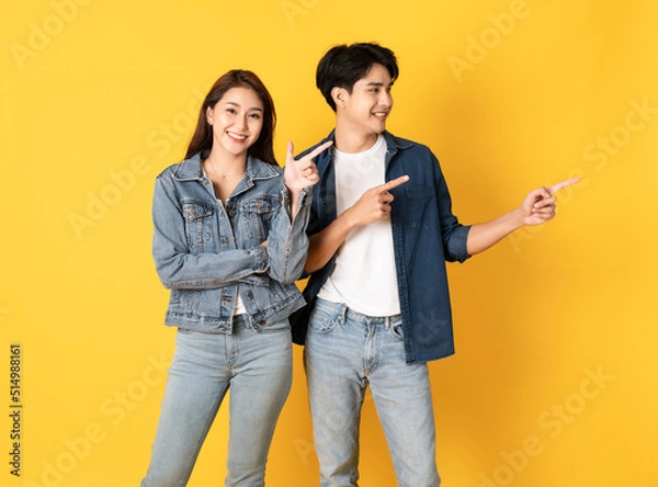 Fototapeta Two Young good looking asian couple using isolated on yellow background presenting to copy space