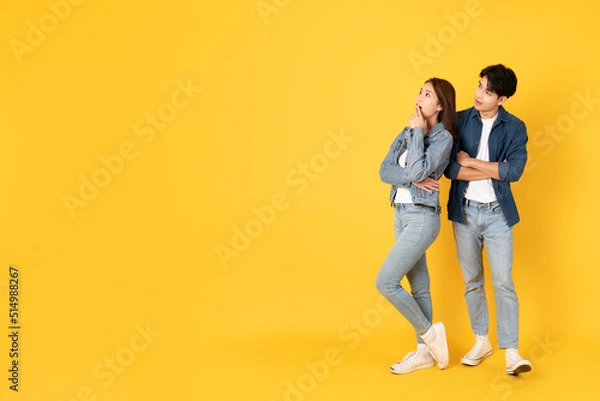 Fototapeta Two Young good looking asian couple using isolated on yellow background presenting to copy space feeling excited