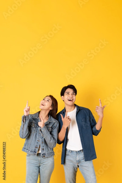 Fototapeta Two Young good looking asian couple using isolated on yellow background presenting to copy space feeling excited