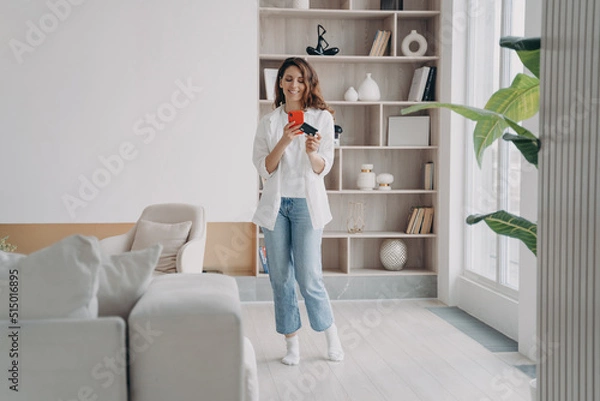 Fototapeta Attractive hispanic girl is shopaholic. Lady is holding card and going to buy through internet.