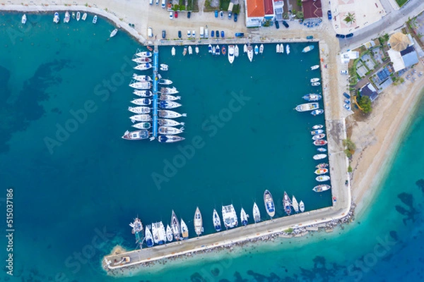 Fototapeta Aerial top-down view of docked sailboats. Top down view of yachts in the marina. Sailboats and regular Boats moured in Palairos Marina Greece. Sailboats and catamarans anchored in the harbour.