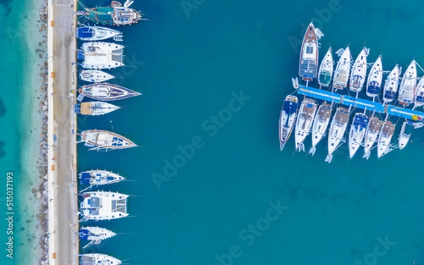 Fototapeta Aerial top-down view of docked sailboats. Top down view of yachts in the marina. Sailboats and regular Boats moured in Palairos Marina Greece. Sailboats and catamarans anchored in the harbour.