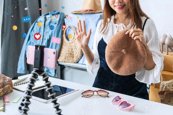 Fototapeta Young Asian woman entrepreneur talking camera live recording video on social network at home. Online selling, work at / from home, Social media and technology concept