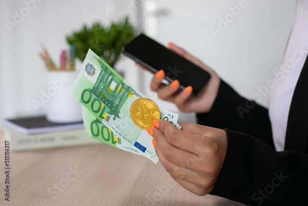 Obraz Euro bills and bitcoin at woman hands with phone in workplace