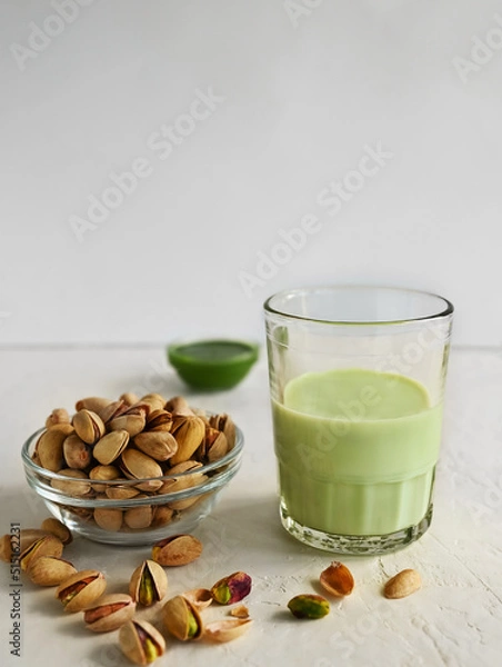 Fototapeta Pistachio milk in the glass and pistachio paste  on the white background. This milk is a great source of antioxidants, phytosterols, and heart healthy fats