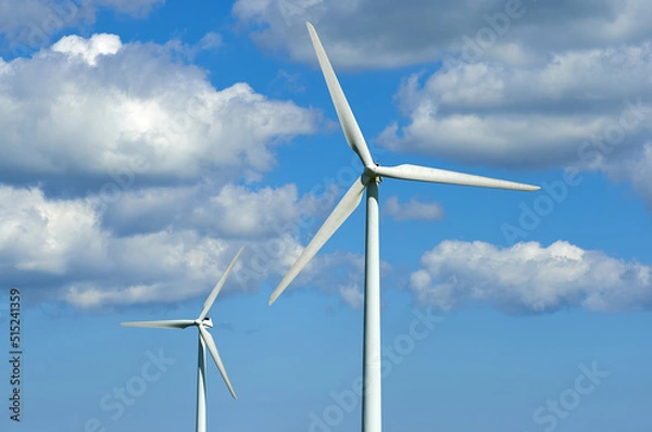 Fototapeta Wind turbines and environmental infrastructure isolated against blue sky with copy space on empty energy farm. Propellers converting sustainable energy into electric power in remote and rural area