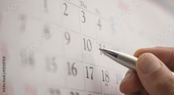 Fototapeta Hand holding a pen and pointing with finger to a monthly calendar
