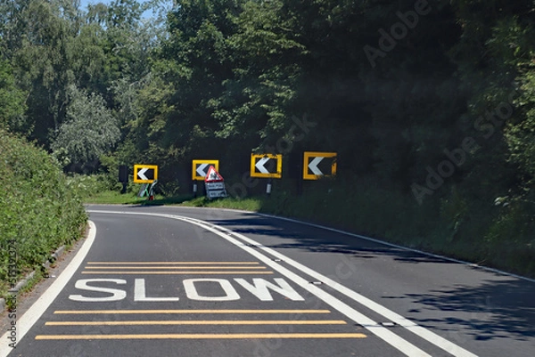 Fototapeta Black and white chevrons, a double white line and a skid risk warning sign tell drivers to slow down because there is danger ahead around the curve