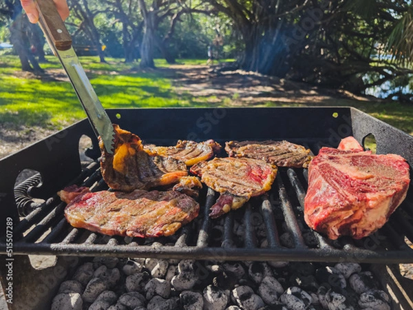 Fototapeta There is meat on the grill. The man turns the meat over. Weekend. Soft focus