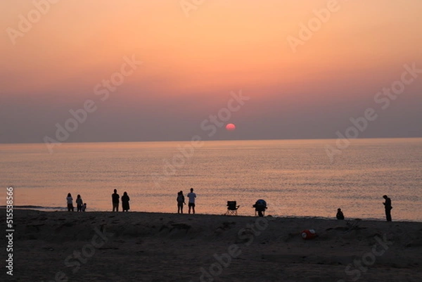 Obraz 海に沈む夕日を見る人々