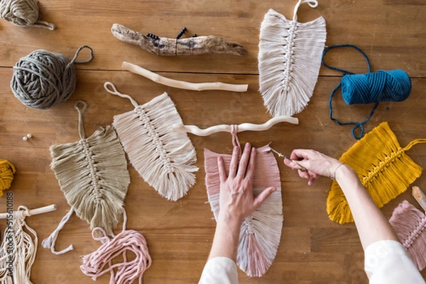 Obraz Top view of woman creating macrame on wooden table. Female hands cutting macrame feathers or leaves.