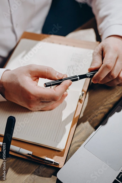 Fototapeta A middle-aged family doctor with a beard works in a clinic. A successful senior doctor in a white lab coat writes down the data in a notebook.