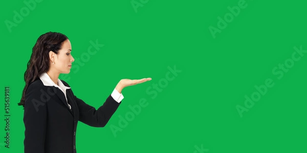 Fototapeta Profile side of beautiful businesswoman showing something or copy spase for product. Brunette woman looking at her hand in business studio concept, isolated on vivid green background.