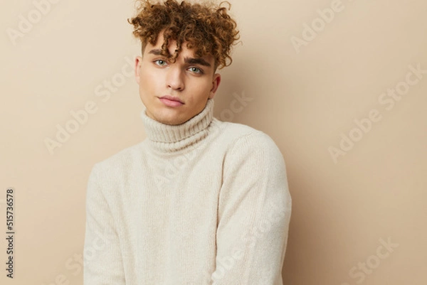 Fototapeta a close horizontal portrait of a handsome, handsome man standing on a beige background in a light turtleneck, looking pleasantly into the camera