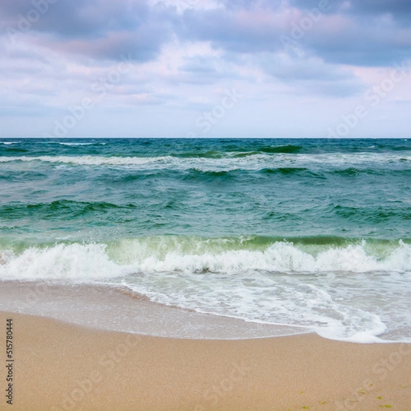 Fototapeta sandy beach before the storm. evening scenery with heavy clouds in colorful light. turquoise waves rushing on the shore. windy weather