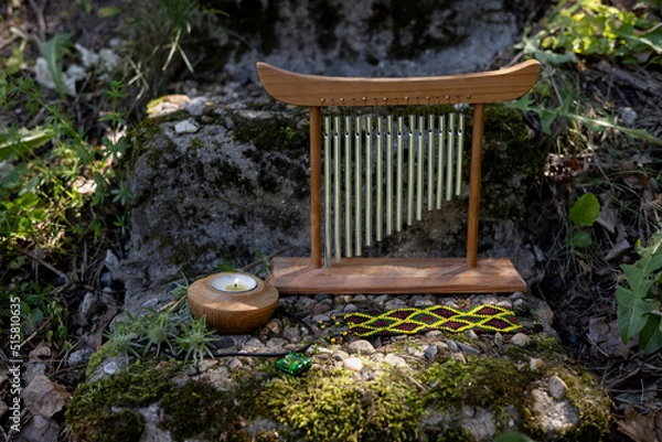 Fototapeta Shamanic paraphernalia chimes wind music, candle, bracelet lie on an old mossy slab