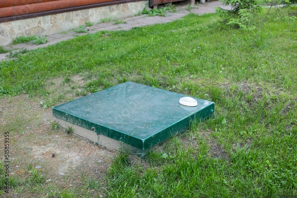 Obraz Square metal cover of an autonomous septic tank with a warning lamp on the lawn next to the building. Sewer system of the house