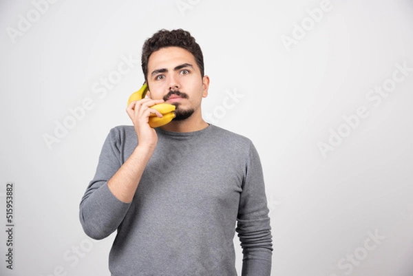 Obraz Serious male talking with banana on gray background