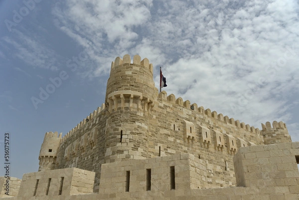Fototapeta Citadel of Qaitbay, Alexandria, Egypt with the Egyptian flag on top and a background of blue cloudy sky. The Fort of Qaitbay is a 15th-century defensive fortress located on the Mediterranean sea coast