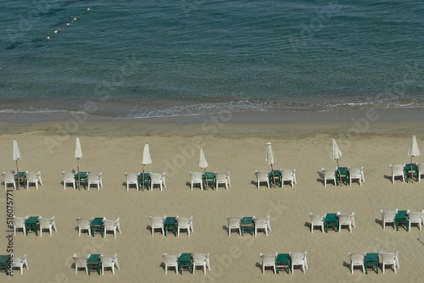 Fototapeta Arrangement of umbrellas, tables, and chairs on a sandy beach in Alexandria, Egypt, on the mediterranean sea. Background of sea waves.