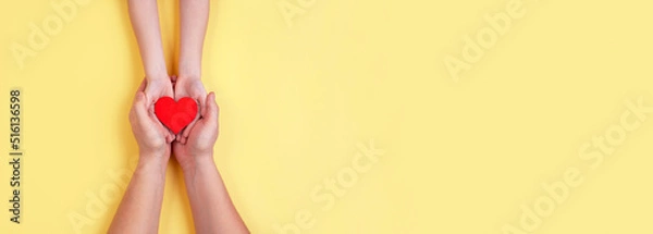 Fototapeta A red wooden heart is held in the hands of a child and a man. Holiday Valentine's Day.