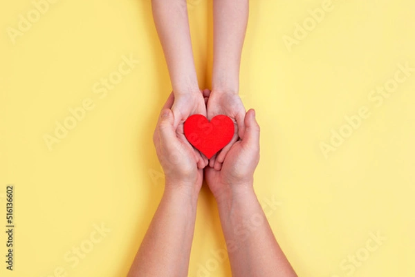 Fototapeta A red wooden heart is held in the hands of a child and a man. Holiday Valentine's Day.