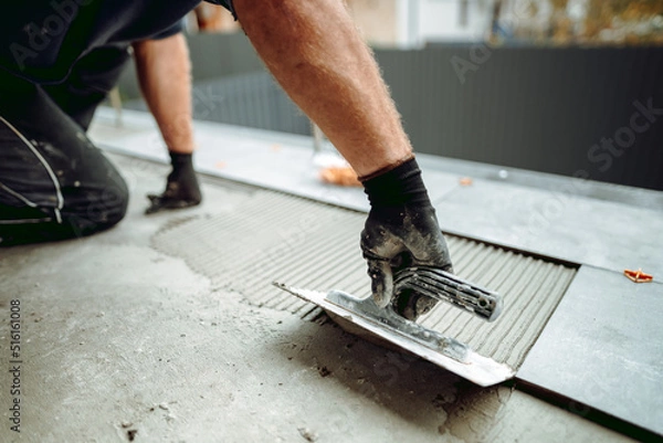 Fototapeta Flooring and tiling. Hand of professional construction worker placing floor tiles on adhesive surface on balcony