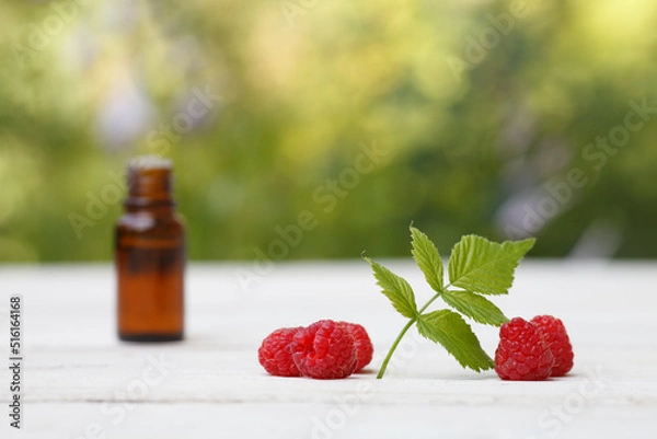 Fototapeta Red Raspberry (rubus idaeus) seed oil bottle with red raspberry and leave on white wooden and greenery background
