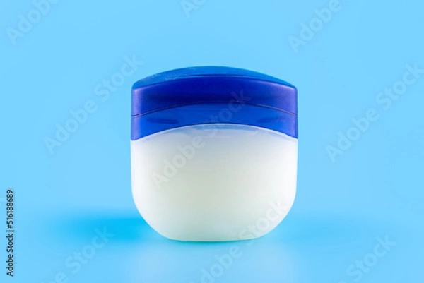 Fototapeta Vaseline or petroleum jelly in a clear jar on blue background with copy space for text. Skin care ointment