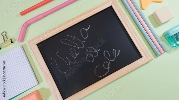 Fototapeta School blackboard with handwritten "back to school" text. School material all around on green background.