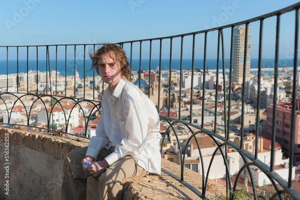 Obraz Young man in a white shirt looking at the camera with the city of Alicante in the background