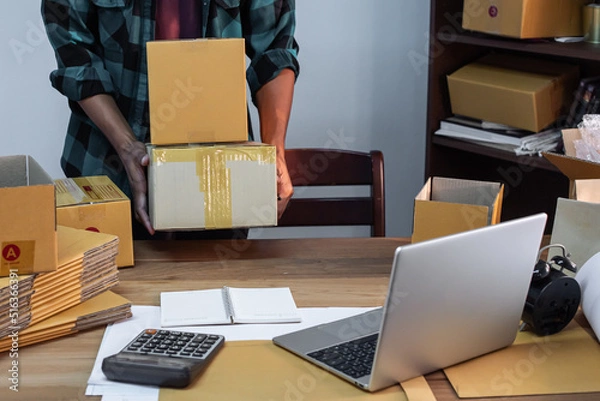 Fototapeta Small business owner packing in the cardbox at workplace. Cropped shot of man preparing a parcel for delivery at online selling business office. Ecommerce drop shipping shipment service concept.