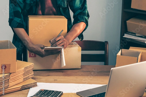Fototapeta Young entrepreneur business owner work at home, small business startup receive order client and take note working with report and pack the product on purchase delivery online to sending destination.