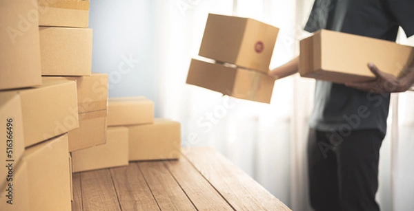 Fototapeta Small business owner packing in the cardbox at workplace. Cropped shot of man preparing a parcel for delivery at online selling business office. Ecommerce drop shipping shipment service concept.